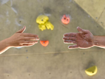 Zwei Menschen reichen sich die Hand vor Kletterwand